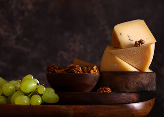 assorted cheeses on a wooden board with green grapes