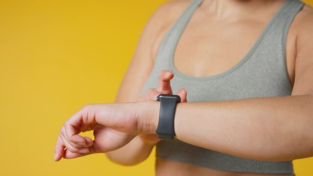 Studio shot of woman in gym fitness clothing streaming to wireless ear buds from smart watch against yellow background - shot in slow motion