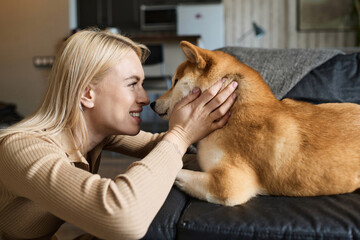 Obraz premium Happy caucasian girl squeezing muzzle of her dog lying on couch at home