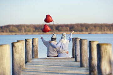 verliebtes Paar am See mit roten Herzballons - obrazy, fototapety, plakaty