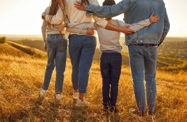 Back view cropped photo of family hugging and looking into the distance enjoying sunset and...