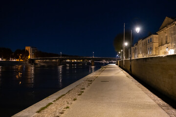 Illuminated quays of the Rhône River by night in Arles, France.