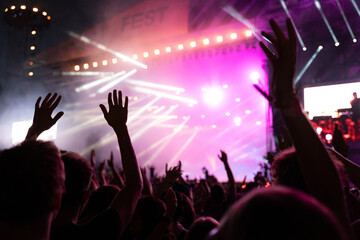 Crowd of people attending a musical performance with hands up in the air. Bright pink light rays coming from the stage