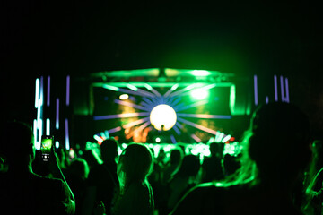 Crowd of people attending a musical performance with hands up in the air. Bright green light rays coming from the stage