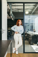 Confident ginger-haired businesswoman contemplating work in office setting