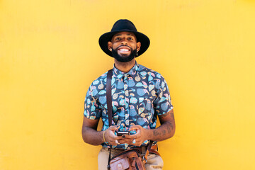 Stylish black man using smartphone outdoors over yellow background