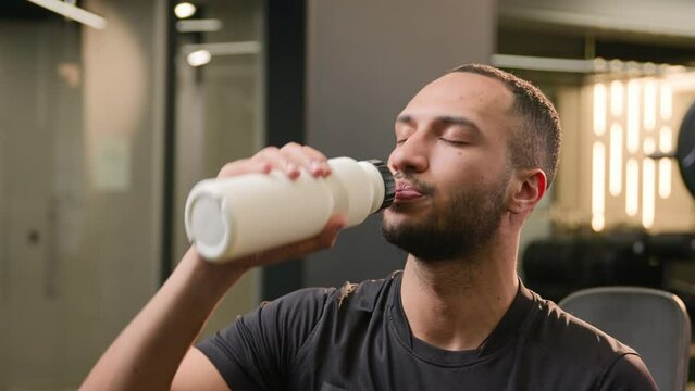 American multiethnic guy sportsman drink refresh after workout sport man sporty male instructor drinking water with fitness bottle relax active exercise fit in gym smiling at camera healthy lifestyle