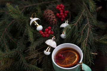 a hot cup of orange tea. Branches of a green fir tree with New Year's toys and red viburnum berries