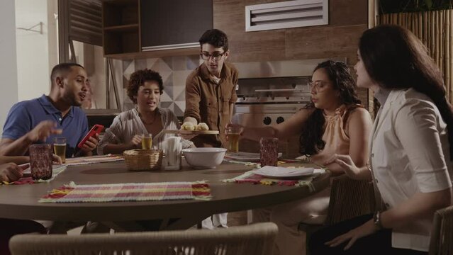 Jovem servindo seus convidados, na cozinha de sua casa. Cinematico 4k.