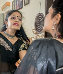 Beautiful Indian woman in black saree and Indian jewelry looking in the Mirror . Portrait of a...