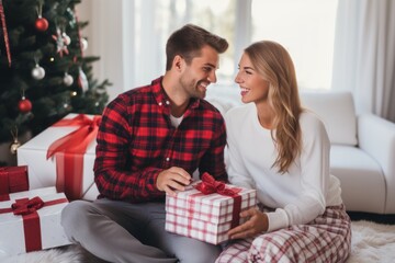 Obraz na płótnie Canvas Young happy couple wearing Xmas pajama plaid bottoms shirts sit in living room and celebration Christmas at home.