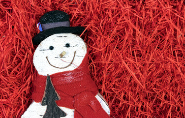 Snowman in a hat and scarf on a background of red shavings.