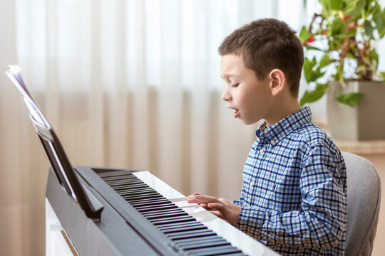 Boy Playing Piano. Little Boy Child Having fun with Learning to Play Piano and Sings Song at Music School. Piano Lessons.