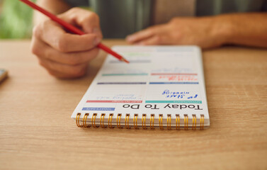 Close up photo of business man hands writing to do list in plan schedule calendar sitting at the table. Male person planning daily appointment for week. Time management and planner concept.