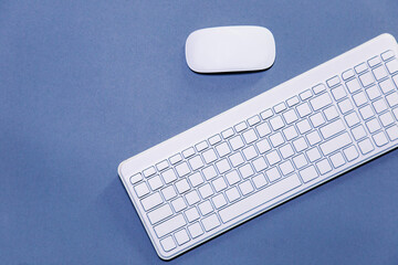 White computer keyboard with white mouse on blue background with copy space, top view, flat lay 
