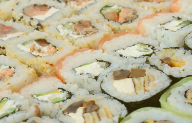 Close-up of a lot of sushi rolls with different fillings lie on a wooden surface. Macro shot of...
