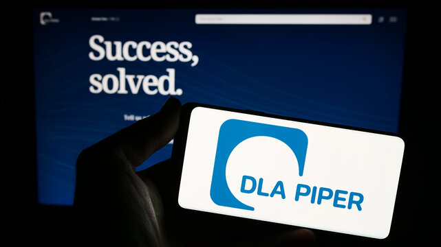 Stuttgart, Germany - 12-17-2023: Person holding smartphone with logo of law firm DLA Piper in front of website. Focus on phone display.