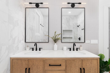 A bathroom with marble and stacked vertical subway tiles, a white oak vanity cabinet, black framed...