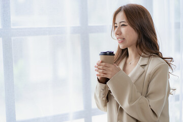 Obraz premium Woman holds a coffee cup and stands near the window to smile with happiness. in the bedroom at home She drinks milk after waking up in the morning.