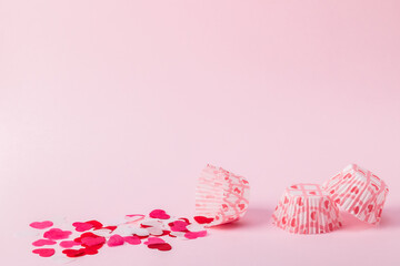 Paper pink cupcake cups with decorative hearts scattered on a pink background. Concept for Valentine's Day, birthday, Mother's Day.