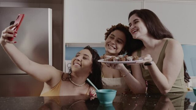 Amigas tirando uma selfie na cozinha, segurando o prato de doces que prepararam juntas. Cinematico 4k.