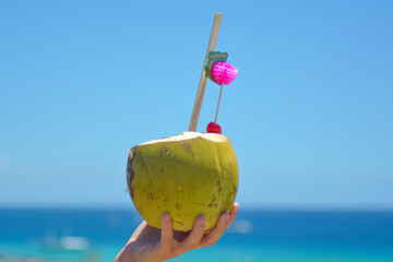 Colourful cocktail in fresh coconut with a straw and pink decoration held in hand. 