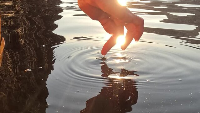 Woman hand sea. Close-up Happy Woman gently caresses water surface at sunset in a warm, golden evening by the sea or lake. Slow-motion Concept of happiness, boat life and holidays in exotic places