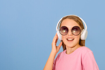 Сheerful girl 10-12 years old wearing headphones. Indicates space for text. Blue background. Copy...
