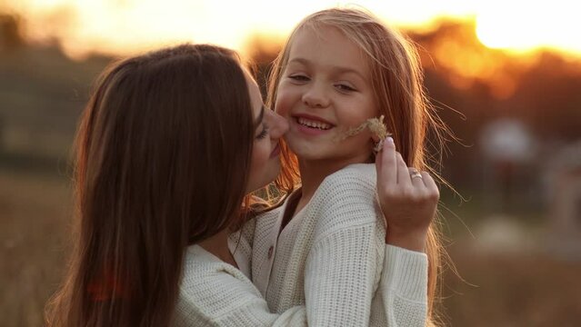 Family day, mother's day. Happy smiling young mom and adorable child daughter soft hugging, kissing and spending time together at autumn on sunset. Idyllic family having fun outdoors on fall holiday