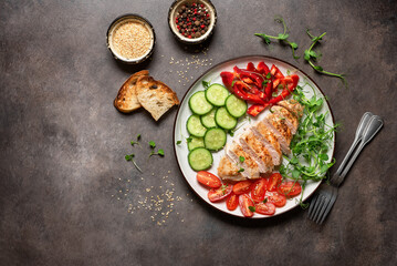 Grilled chicken fillet with fresh vegetables on a dark rustic background. Top view, flat lay