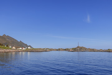 Obraz premium Expansive seascape showcasing traditional red Rorbu cottages along the rugged coastline of Moskenes, Lofoten Islands, Norway, bathed in summer sunshine beneath a clear azure sky