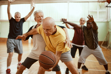 Group of active senior men playing basketball indoor