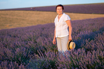Naklejka na ściany i meble A middle-aged woman in a lavender field and enjoys aromatherapy. Aromatherapy concept, lavender oil, photo session in lavender