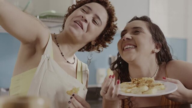 Friends taking a selfie in the kitchen, holding the plate of sweets they prepared together. Cinematic 4k.