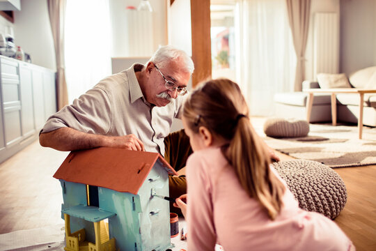 Grandfather painting small toy house with granddaughter at home
