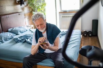 Senior Man Checking Smartphone After Workout in Bedroom