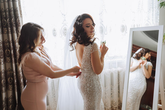 Morning of the bride. The bride's maid of honor helps the bride lace up her dress, fasten buttons on the dress or sleeves. Girlfriends help the bride fasten her dress