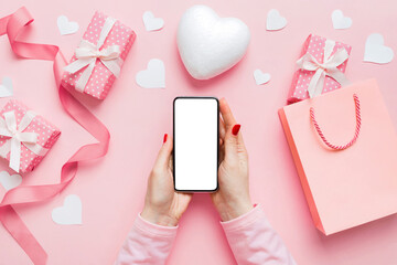 Woman hand holding mobile phone with blank screen on colored background with hearts, valentine day concept top view flat lay