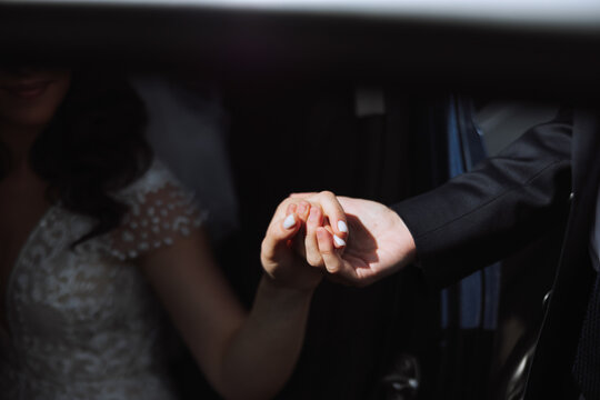 A beautiful bride, sitting in a car, gives her hand to her husband. A beautiful bride with a bouquet of flowers in her hands is sitting in a stylish expensive car.