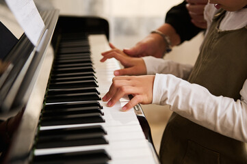 Side view of child's hands on piano keyboard, touching white and black keys while playing music on...