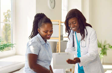 Female friendly doctor talking with a happy smiling african american woman patient sitting on the...