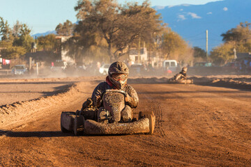 Kart driver full of mud, on the straight of a dirt karting circuit.