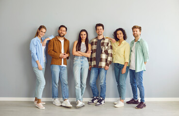 Fototapeta premium Portrait of a group of young happy smiling friends students or colleagues in casual clothes standing together isolated on a grey background and looking confidently and positively at camera.