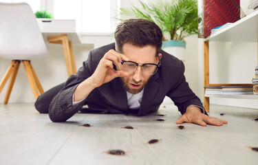 Shocked young business man in suit lying on white floor in his house or office, holding his...