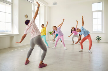 Female young choreographer showing her students girls stretching exercises in dance studio. Happy...