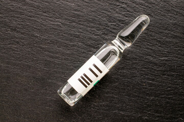 One glass medical ampoule on slate stone, macro, top view.