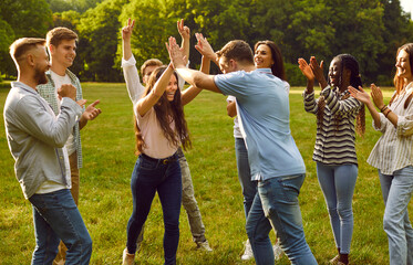 Happy students friends standing together outdoor in summer park having fun in nature and enjoying meeting on holidays. Group of a young people walking in garden and having weekend activity.