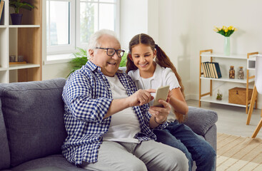 Grandfather and granddaughter spending time together while watching videos or photos on mobile...