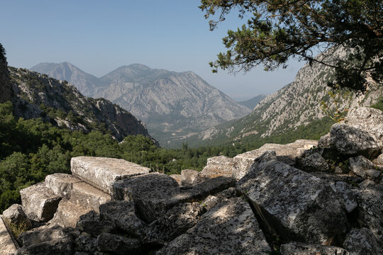 Mediterranean mountain landscape. In the front ancient ruins of massive gray stone platforms. Behind are rocky hills covered with dry green forest