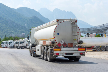 Parking row of trucks with fuel tanks in front of a warehouse and storage of huge tanks of raw...
